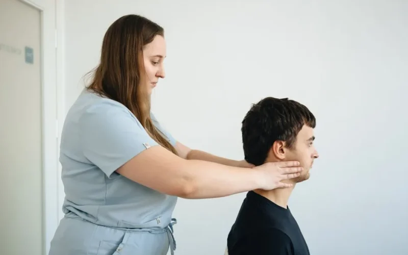 A physiotherapist performs a neck adjustment on a male patient in a clinic setting.
