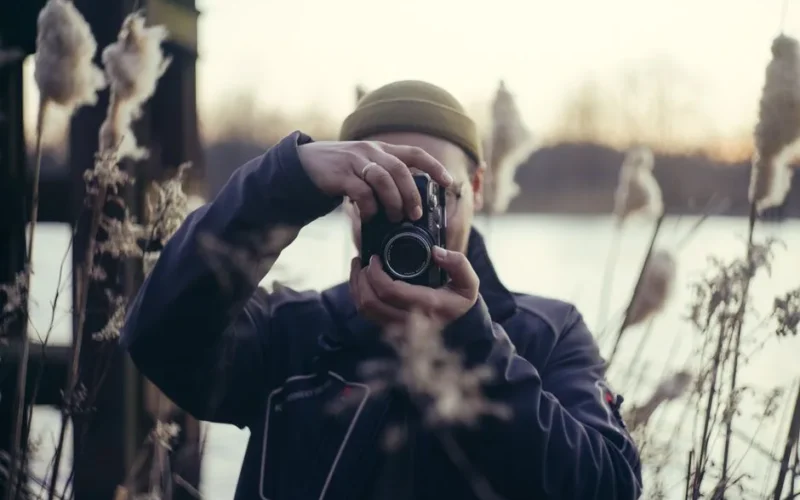 A photographer capturing a scene near a river surrounded by tall grass in Wrocław, Poland.