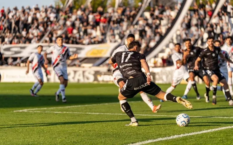 A dynamic football match with players in motion on a sunny day, witnessed by a packed stadium.