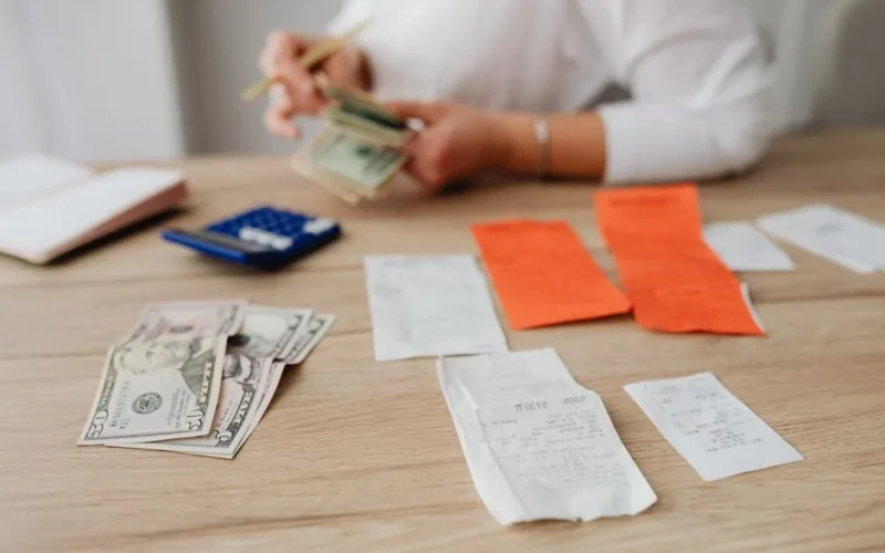 A person using a calculator and cash to plan a household budget.
