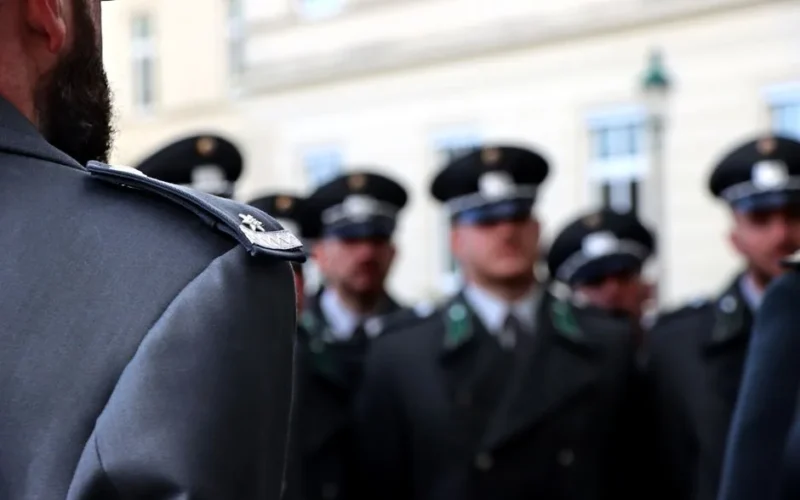 Blurred group of uniformed officers in formation, focusing on insignia and uniform details.
