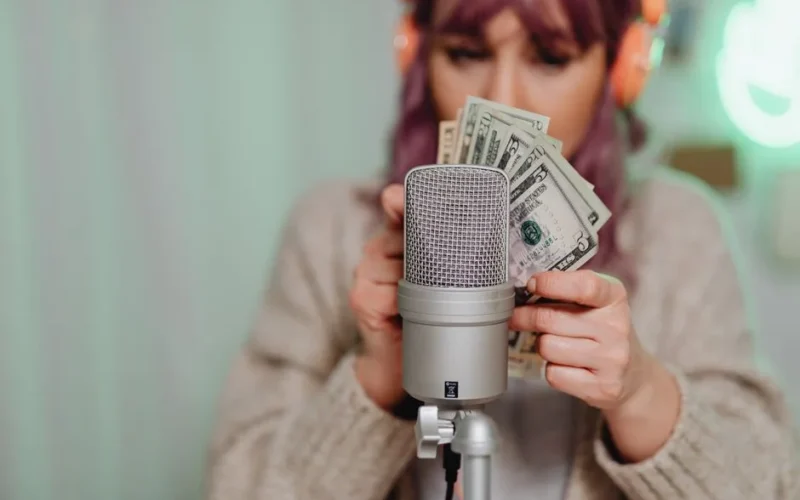 Adult woman with headset counting dollar bills in front of microphone indoors.
