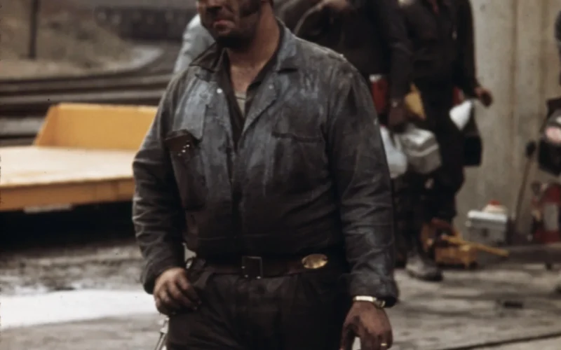 Miner, who has just finished his shift at Virginia-Pocahontas Coal Company mine #4, near Richlands, Virginia carries his empty lunch pail. The brass plate on his belt carries his name and blood type. The belt also holds batteries for his head lamp and life saver breathing apparatus. His yellow hat means he is a safety man. The lamp (partially obscured on his right hip) detects black damp places where there is not enough oxygen for the miners.