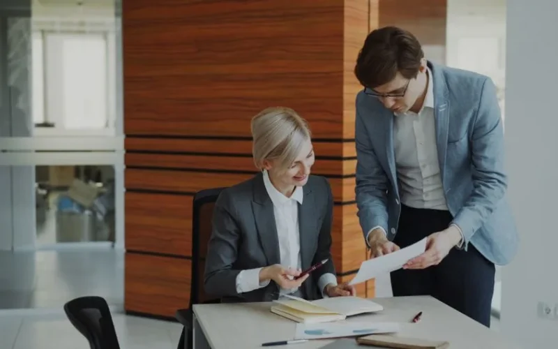 Two professionals discussing documents in a modern office setting.