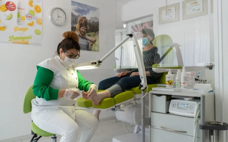 Concentrated professional beauty master in protective mask and gloves doing pedicure in modern salon