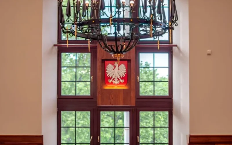 Window with Polish emblem in elegant interior, featuring a stylish chandelier.