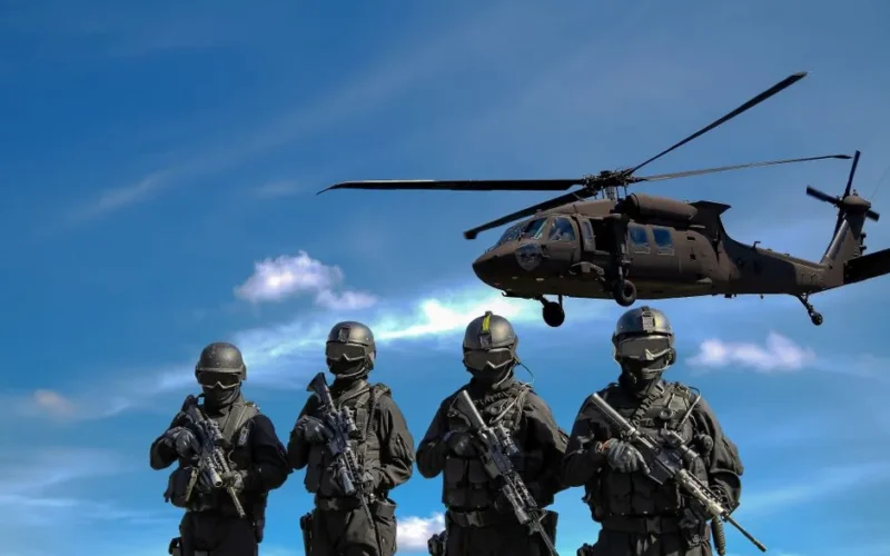 Special forces soldiers in tactical gear with helicopter overhead under a blue sky.