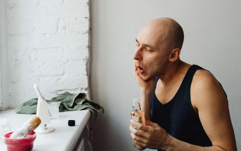 Adult man applying aftershave lotion in a bright bathroom, focusing on skincare routine.