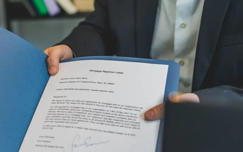 Close-up view of a person holding a mortgage rejection letter in a folder, indoors.