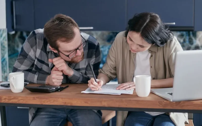 Couple reviewing financial documents together at a kitchen table with a laptop and calculator.