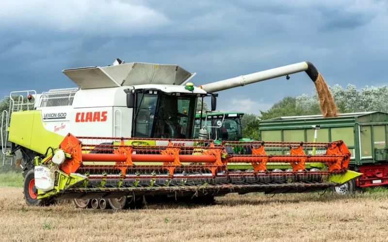 A combine harvester working in a field, unloading grain into a trailer.