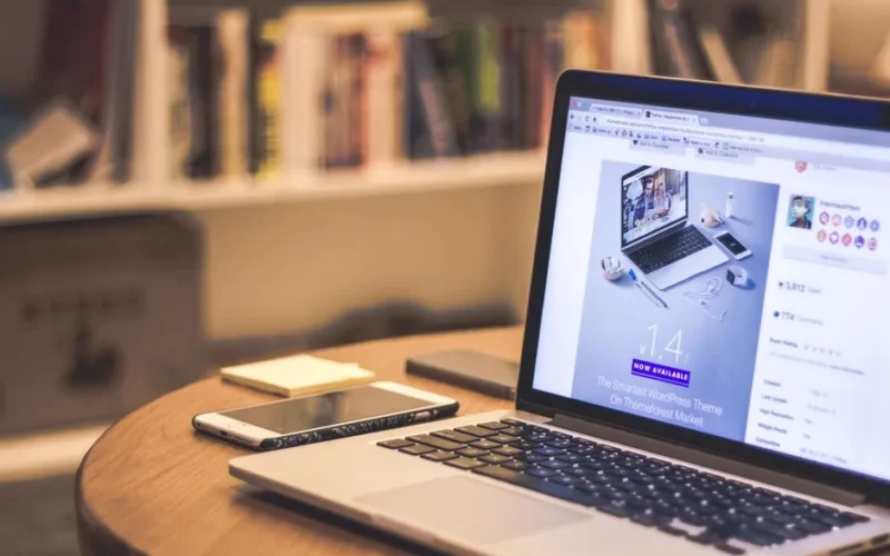 A cozy modern workspace featuring a laptop displaying a website, a smartphone, and books on shelves.