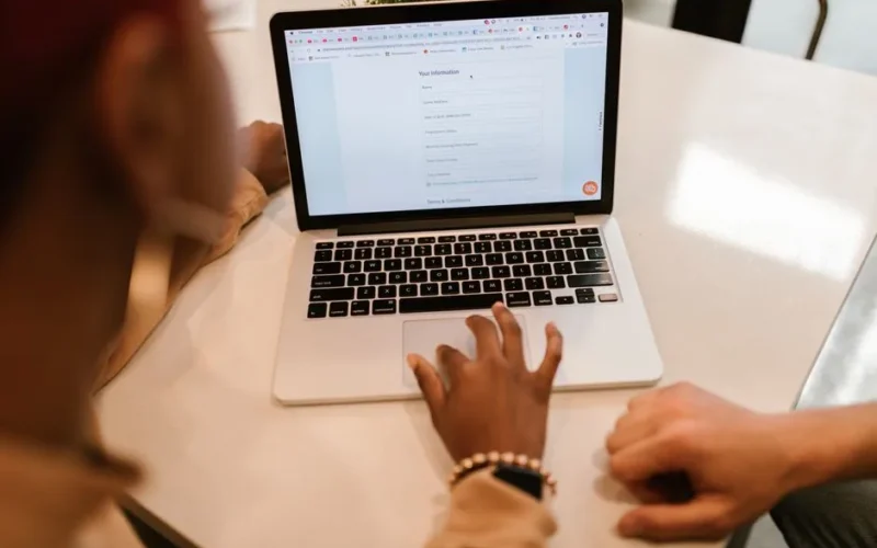 Two adults working together on a laptop displaying an online form, indoors.