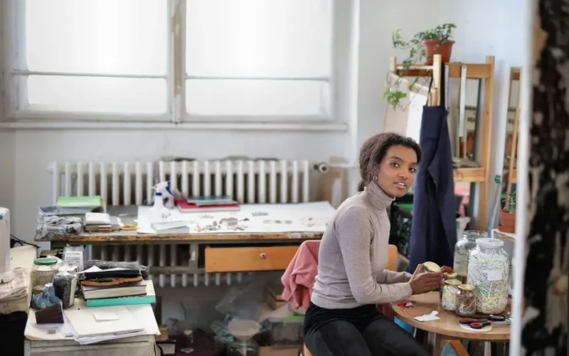 A woman in a creative workspace surrounded by art supplies and plants, exuding creativity and focus.