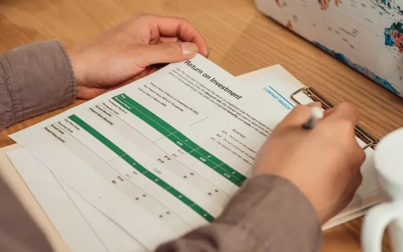 A person analyzing a return on investment report with a pen in hand on a desk.