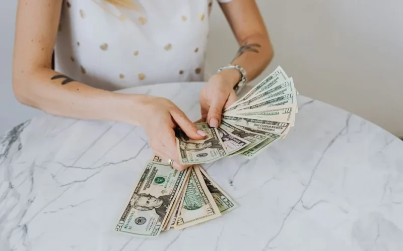 Close-up of a person counting US dollar bills on a luxurious marble table, symbolizing wealth and finance.
