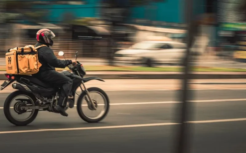 Motorcycle deliveryman speeds through city streets, showcasing fast food service.
