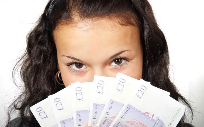 Young woman confidently holding British 20 pound notes. Focus on finance and wealth.