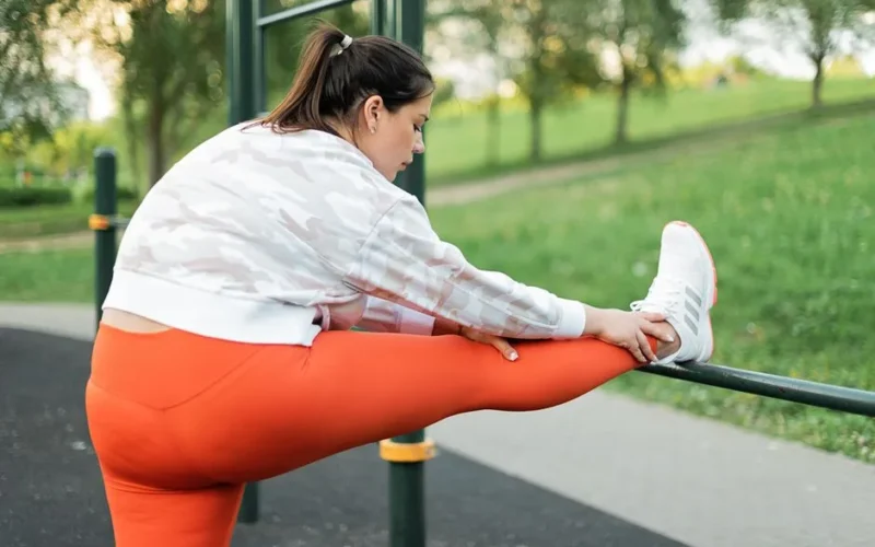 Plus size woman stretching in park wearing orange leggings, promoting active lifestyle and wellness.