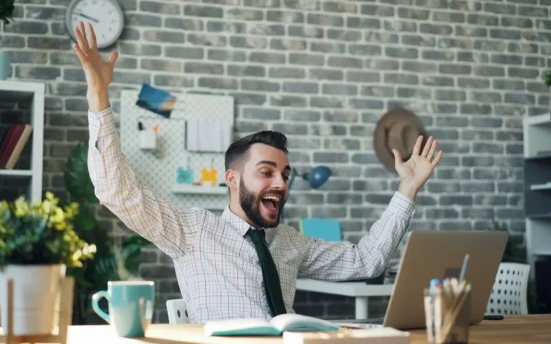 A delighted office worker celebrating success at his desk in a modern office setting.