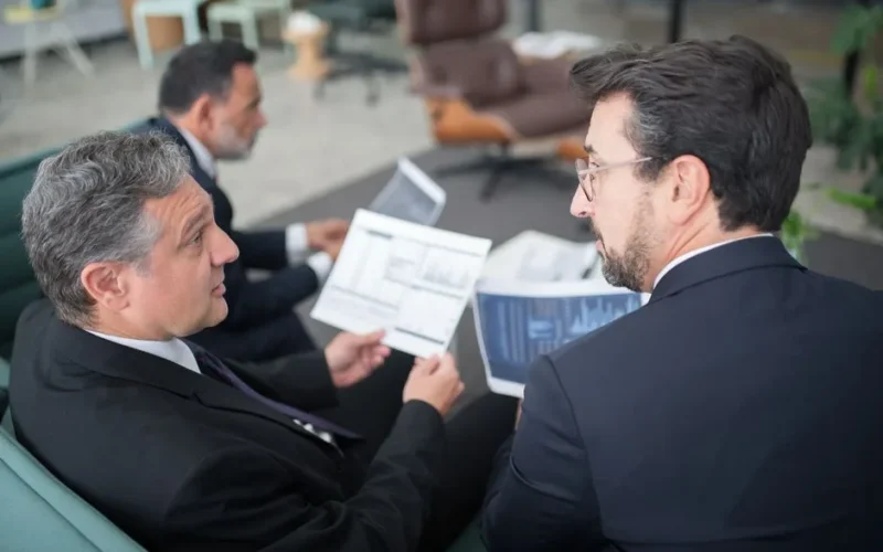Three businessmen discussing financial documents in a modern office setting.