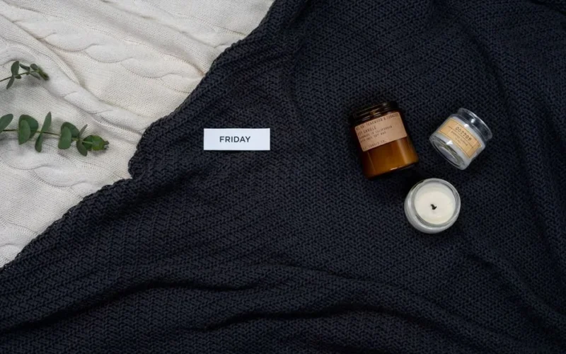Warm knitted blankets with candles and eucalyptus for a cozy Friday ambiance.