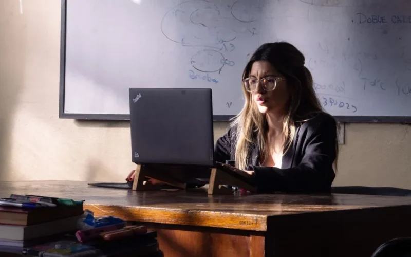 A woman educator focuses on her laptop in a sunlit Buenos Aires classroom, promoting learning and concentration.