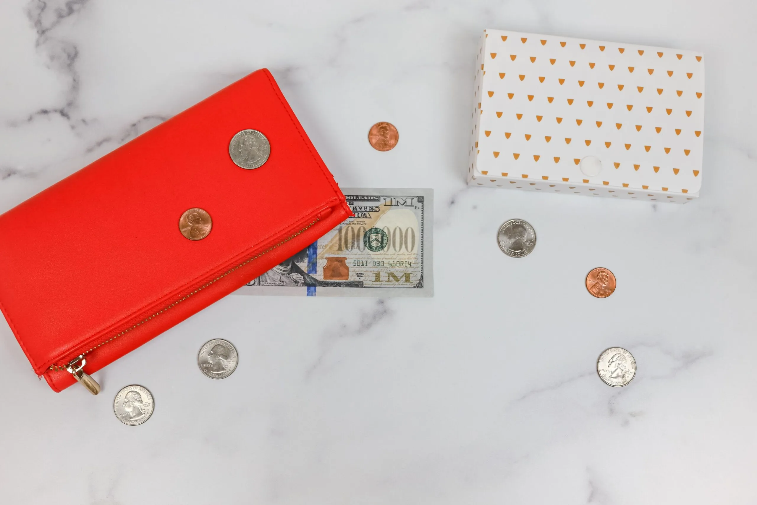Flat lay of red wallet, US dollars, coins, and gift box on marble surface