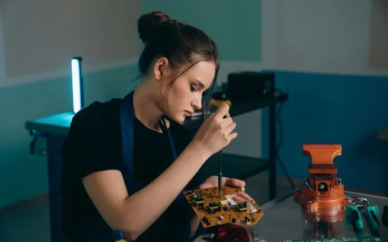 Focused young woman assembling electronics in a workshop setting.