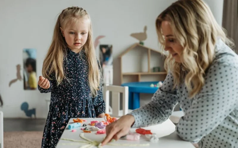 A young girl and a woman engage in a creative activity at a preschool classroom, fostering learning.