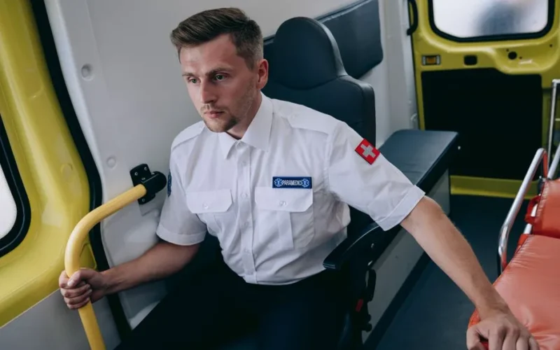 Focused paramedic in uniform sitting inside an ambulance, ready for action.
