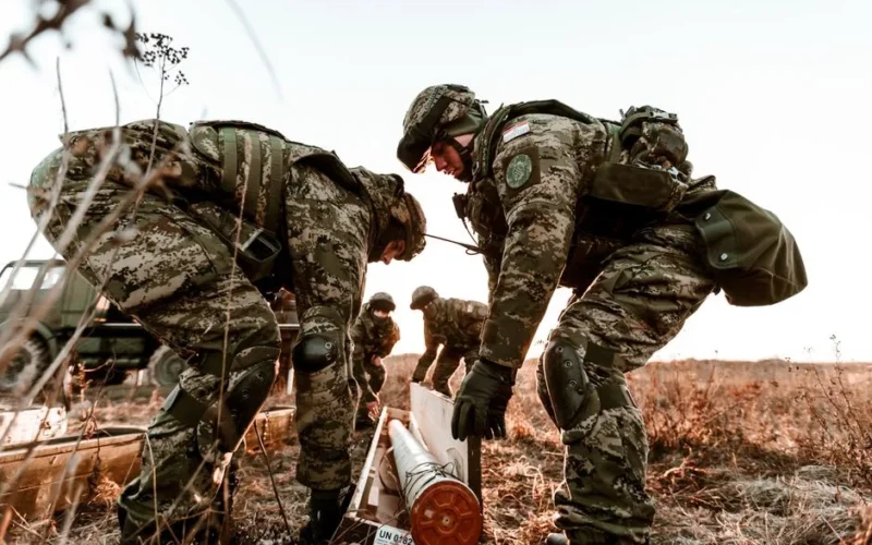 Soldiers in camouflage uniforms during training exercises at sunset in an open field.