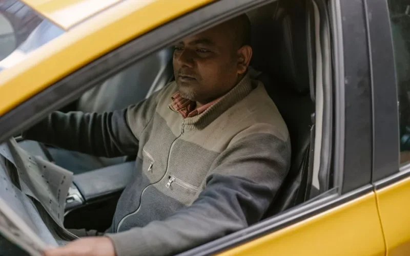 Ethnic male driver reading daily newspaper with interest while sitting in car and having break