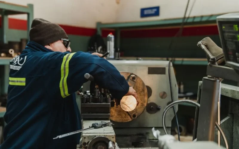 Industrial worker focused on operating a lathe in a busy workshop setting.