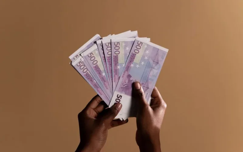 Close-up of hands holding several 500 euro banknotes against a neutral beige background, concept of wealth.