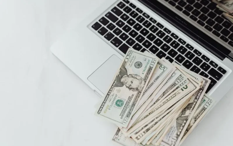 A stack of US dollar bills on a laptop keyboard representing online finance and budgeting.