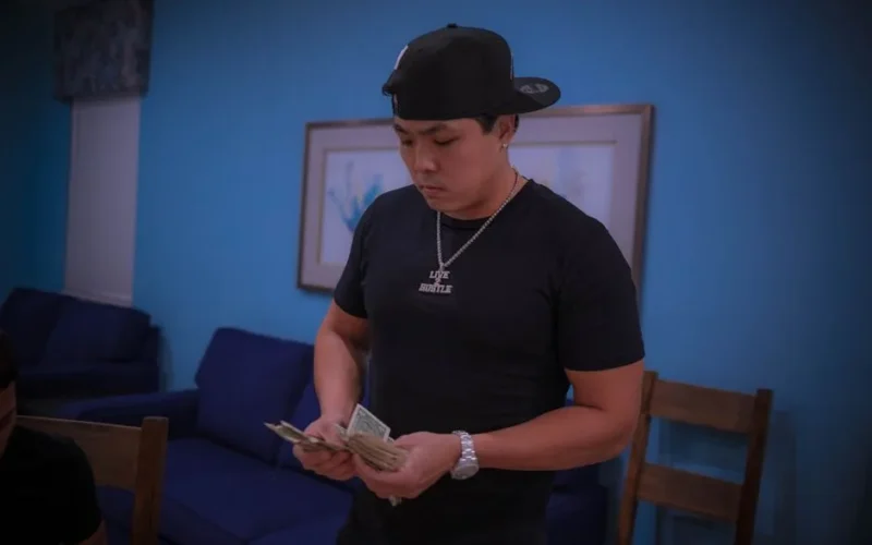 Man in casual attire counts dollar bills in a cozy room setting.