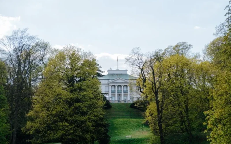 A picturesque view of Belweder Palace in Warsaw surrounded by lush spring foliage.