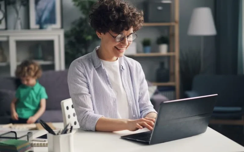 Smiling woman using laptop for remote work in a cozy home setting.