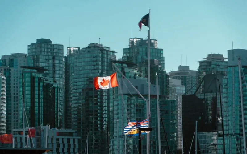 A view of Vancouver's glassy skyscrapers with Canadian and British Columbia flags waving in the foreground.