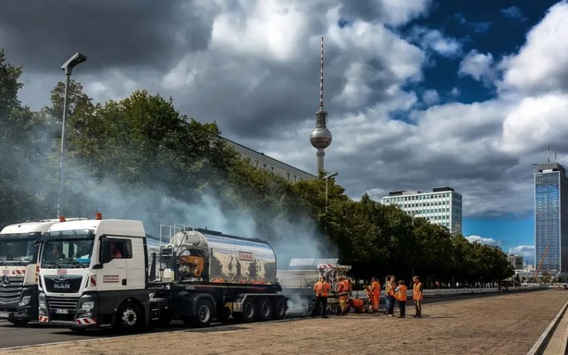 Construction crew working on city street in Berlin with trucks and Berlin TV Tower in backdrop.