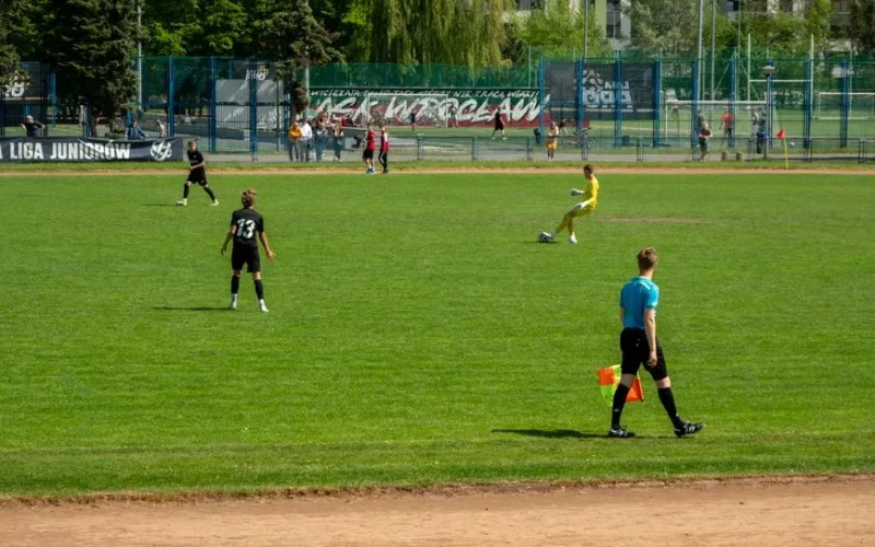 Youth soccer game at Wrocław sports field on a sunny day with players and referee in action.