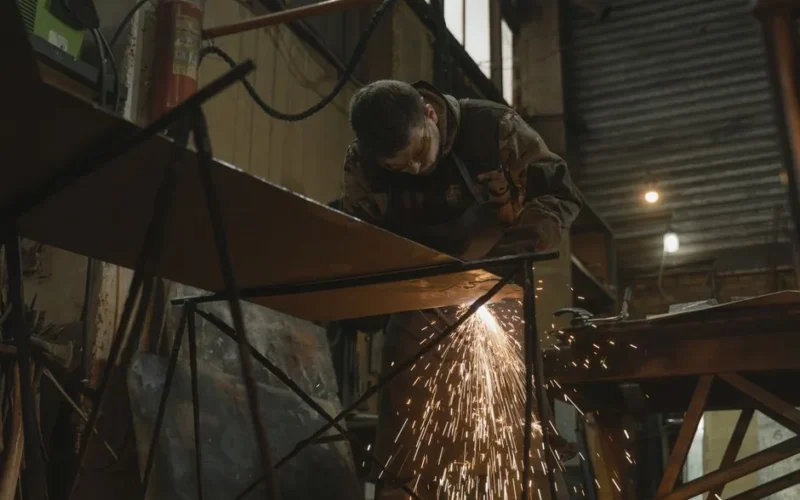 A worker focused on welding metal inside an industrial setting with sparks flying.