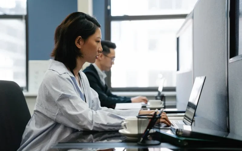 Two professionals working diligently on laptops in a modern office setup, capturing productivity and teamwork.