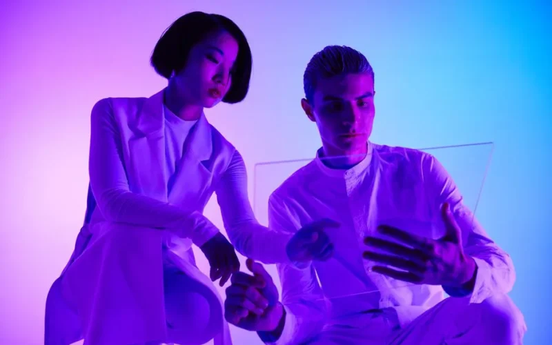 A man and woman engaging with a transparent holographic screen in a modern studio setting.