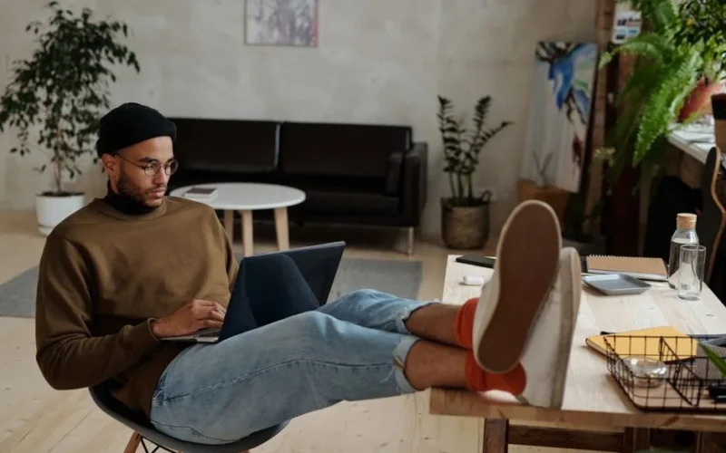 Casually dressed man freelancing with laptop in stylish, plant-filled home office.