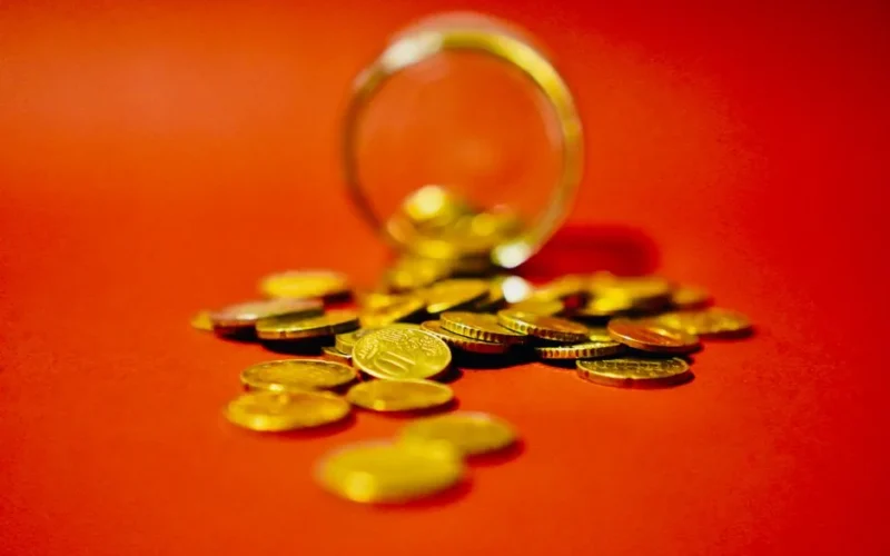 A collection of golden coins spilling from a glass jar on a vibrant red background symbolizes wealth.