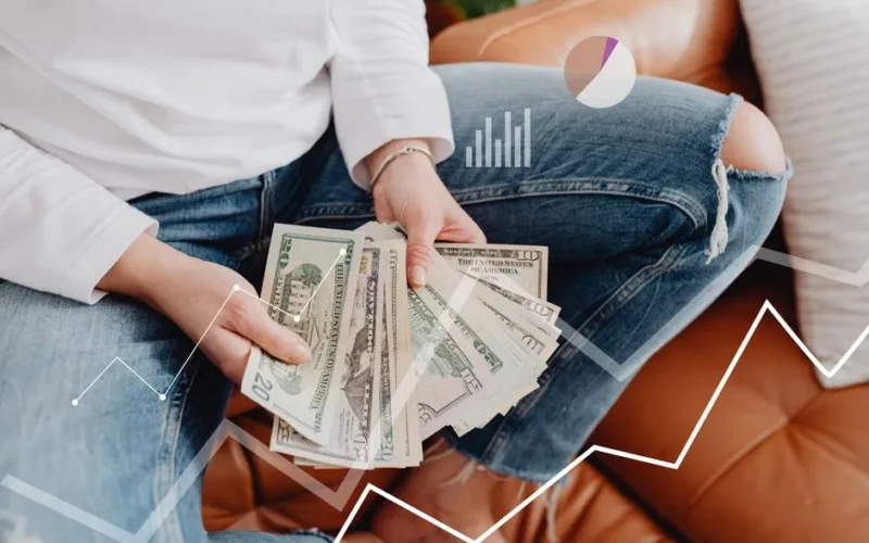 Person with dollars in hand, sitting, financial graphics overlay showing growth.