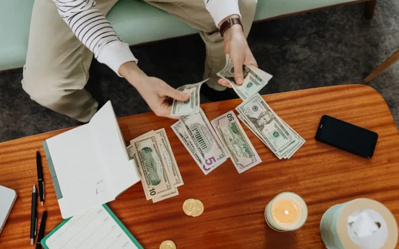 A person sitting and counting various US dollar bills at a table indoors.