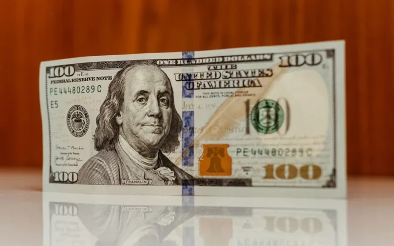 Crisp image of a $100 bill standing and reflecting on a smooth surface, highlighting details.